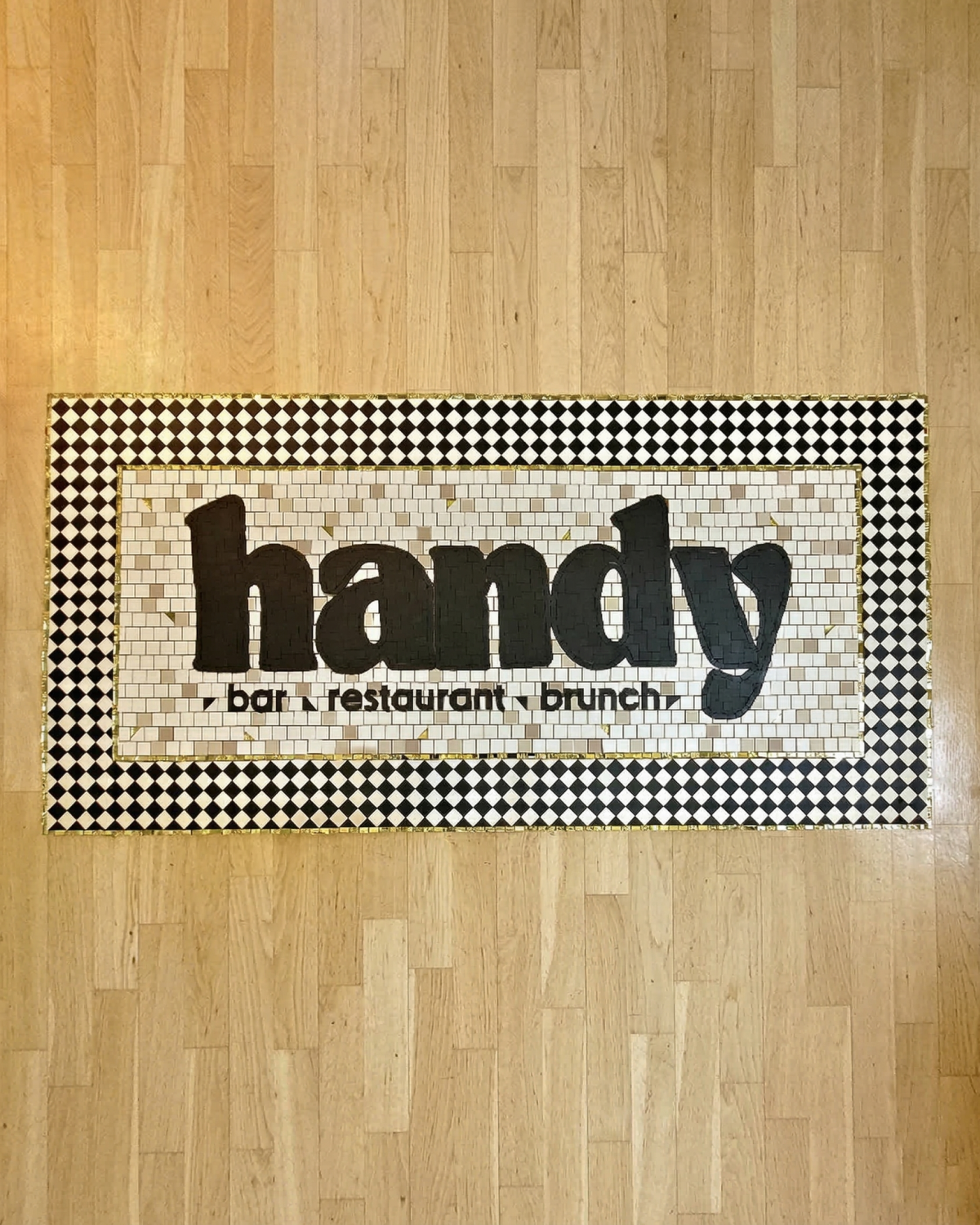 Zoom tapis mosaïque artisanale lettrage Handy bar restaurant brunch · tesselles noires sur fond blanc · bordure damier · La FABMOZ Nantes