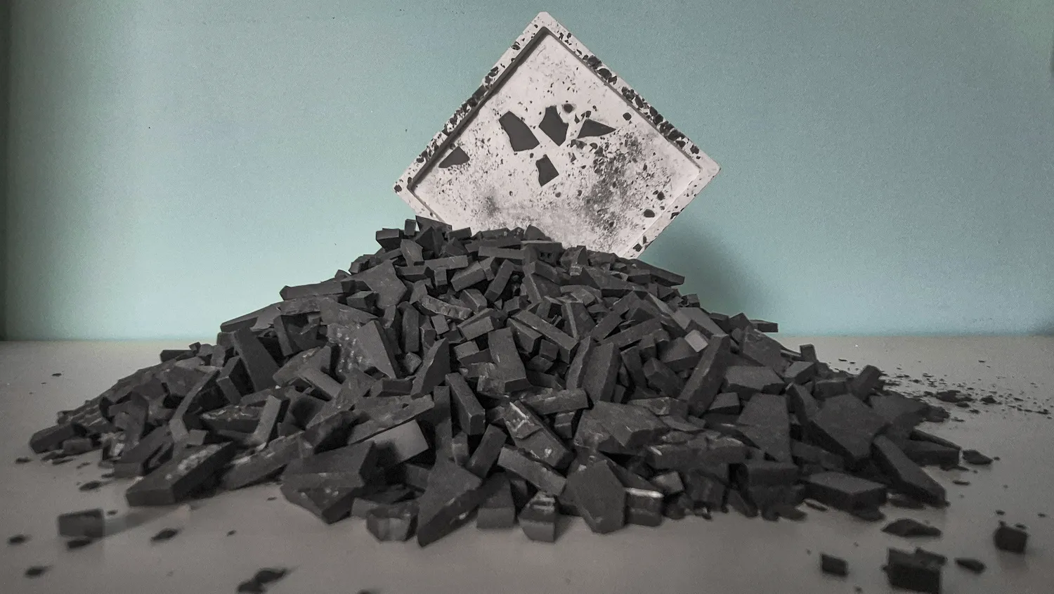 Prototype de tesselle en terrasso recyclé posé sur un tas de granulat noir · matière première R&D MATMOZ · La FABMOZ Nantes