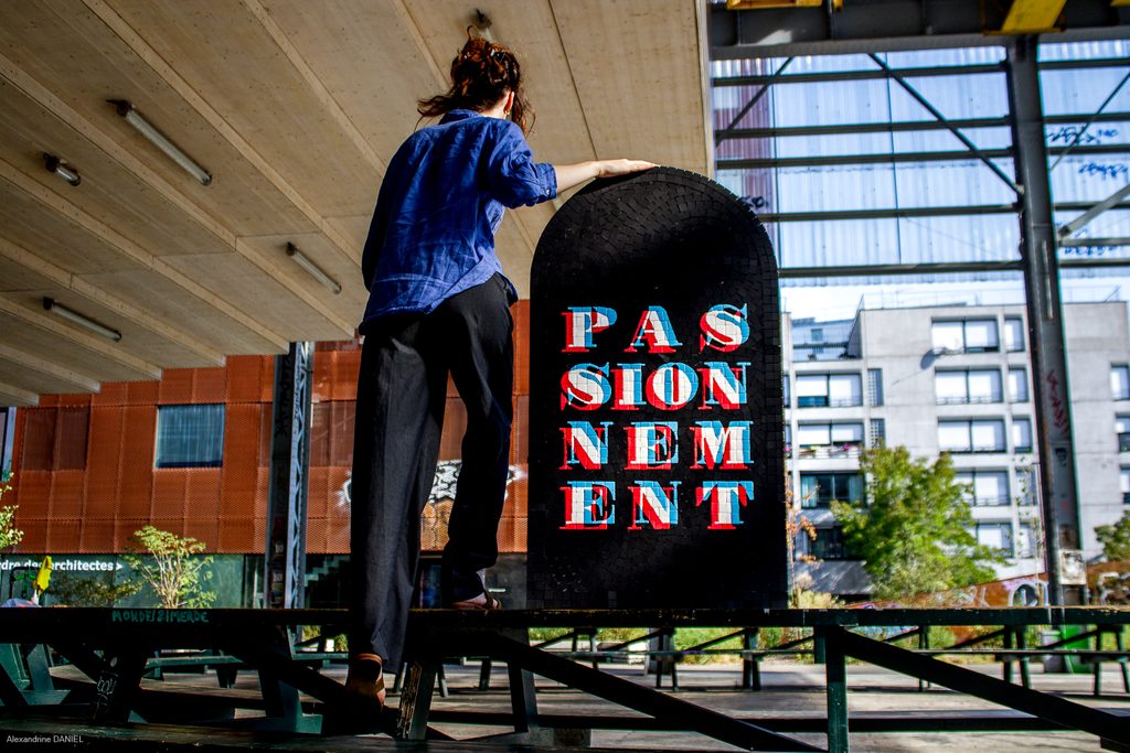 Chloé Gunet-Caplain présentant la mosaïque Passionnément, création La FABMOZ en grès cérame noir, lettrage typographique en émaux de Briare, style graphique anaglyphe